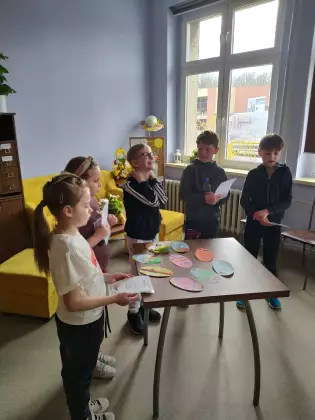 Dzieci stoją przy stoliku na którym leżą wielkanocne pisanki.