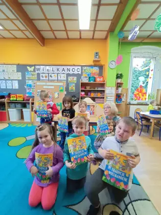 Dzieci siedzą na dywanie trzymając w rękach nagrody za konkurs.