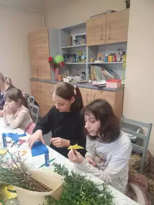 Dziewczyny siedzą przy stole i wycinają kokardy z filcu.