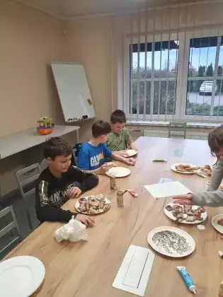 Chłopcy siedzą przy stole i jedzą upieczone pierniczki.
