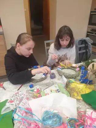 Dziewczyny siedzą przy stole i owijają wianki wielkanocne.