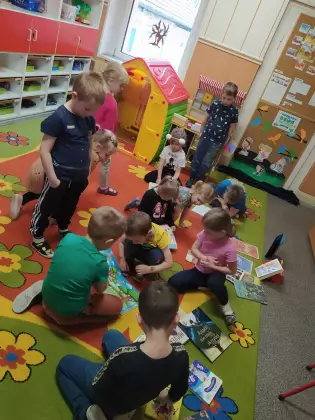 Przedszkolaki na dywanie oglądają książeczki.