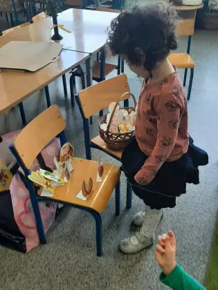 Dziewczynka wkłada do koszyka wielkanocnego pokarm wycięty z papieru.