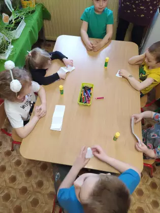 Dzieci siedzą przy stoliku i wykonują pracę plastyczną.