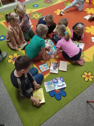 Przedszkolaki na dywanie oglądają książeczki