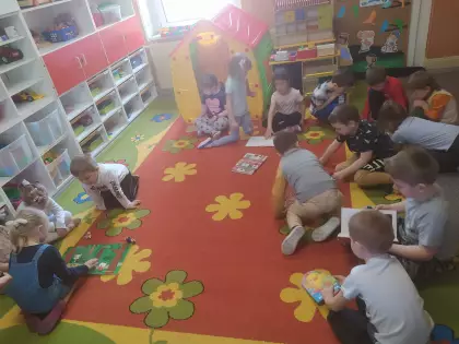 Dzieci siedzą na dywanie w przedszkolu i oglądają książki.