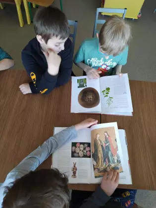 Dzieci siedzą przy stole i oglądają książkę.