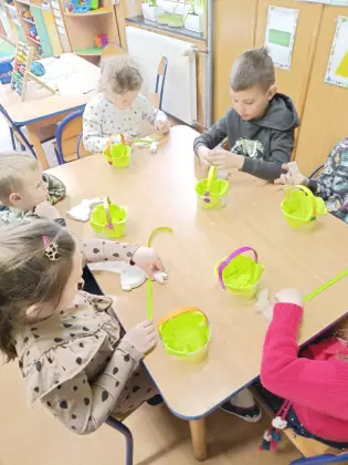 Dzieci siedzą przy stoliku i wykonują koszyczki wielkanocne.