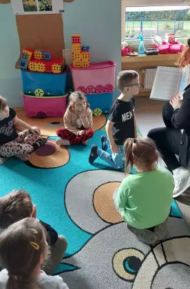 Dzieci siedzą na dywanie i słuchają baśni Księżniczka na ziarnku grochu.