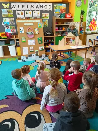 Dzieci siedzą na dywanie i słuchają opowiadania w formie teatrzyku.