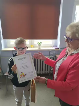 Bibliotekarka wręcza dyplom za udział w konkursie wielkanocnym.