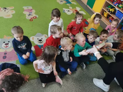 Maluszki siedzą na dywanie i oglądają książeczki.