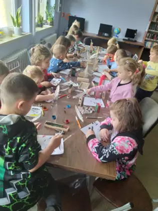 Uczestnicy siedzą przy stole i wykonują prace plastyczne.