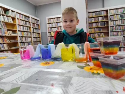 Chłopczyk siedzi przy stole. przed nim stoją szklanki wypełnione kolorowym płynem.