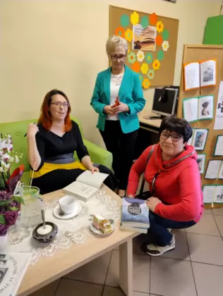 Autorka podpisuje dedykacje w książkach. Obok stoją dwie Panie.