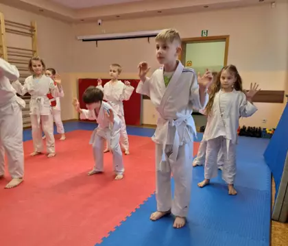 Uczestnicy wspólnie z trenerem ćwiczą przysiady.