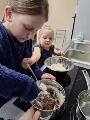 Uczestniczki zajęć robią czekoladę. Jedna miesza w garnku składniki a druga dosypuje kolejne.