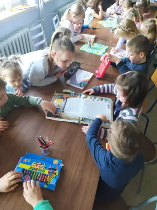 Przedszkolaki siedzą przy stoliku i oglądają książeczki dla dzieci.