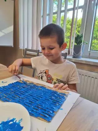 Uczestnik zajęć maluje obraz niebieską farbą.