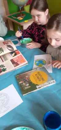 Dziewczynka miesza farbę w misce a druga ogląda książeczkę.