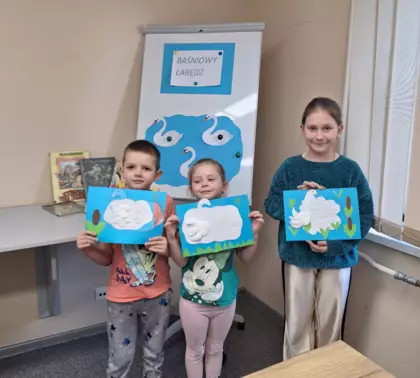 Wspólne zdjęcie po zajęciach plastycznych. Troje dzieci trzyma w rękach prace plastyczne - łabędzia wykonanego z płatków kosmetycznych.