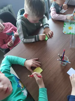 Przedszkolaki wykonują prace plastyczną - małe kolorowe książeczki.