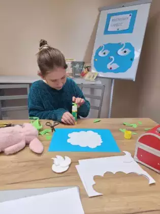 Dziewczynka wykonuje pracę plastyczną - łabędzia z płatków kosmetycznych.