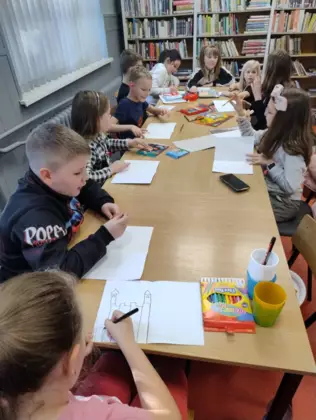 Uczestnicy przy dużym stole wykonują prace plastyczne.