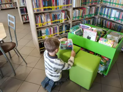 Przedszkolak oparty o pufkę ogląda książeczkę.