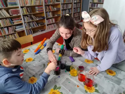 Dwie dziewczyny i chłopak tworzą tęcze z bibuły i szklanek z kolorowym płynem