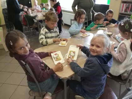 Przedszkolaki siedzą przy stoliku i częstują się urodzinowym tortem.