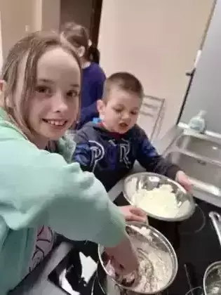 Uczestniczka zajęć miesza składniki na czekoladę w garnku a chłopczyk dosypuje łyżką kolejny składnik.