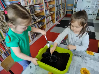 Dziewczynki sadzą rośliny do doniczek.