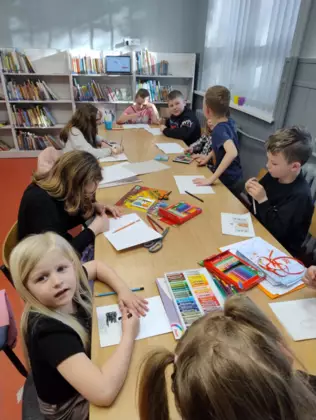 Uczestnicy przy dużym stole wykonują prace plastyczne.