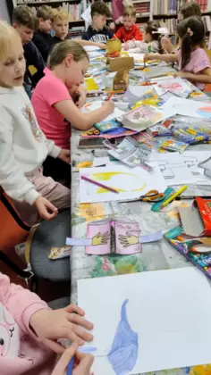 11Dzieci siedzą przy stole i kolorują kredkami.