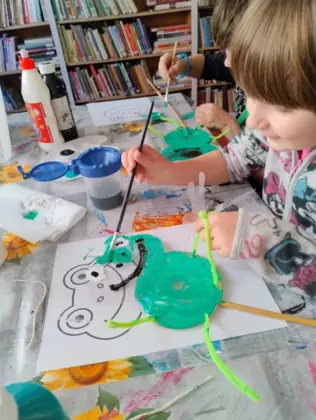 Dzieci malują zieloną farbką żabki z papieru.