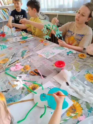 Dzieci malują zieloną farbką żabki z papieru.