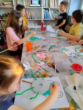 Dzieci malują zieloną farbką żabki z papieru.