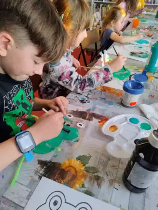Dzieci malują zieloną farbką żabki z papieru.