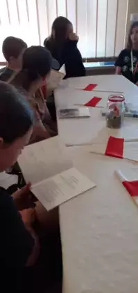 Dzieci czytają książkę na stole leżą flagi z papieru.