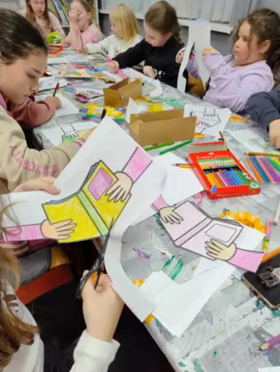 Dzieci siedzą przy stole i kolorują kredkami.