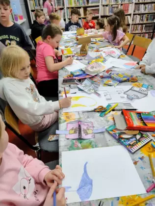 Dzieci siedzą przy stole i kolorują kredkami.