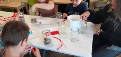 Dzieci słoiki wysypują kamieniami i przyklejają na nie flagi Polski.