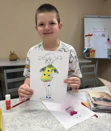 Uśmiechnięty chłopczyk trzyma w rękach pokolorowany obrazek.