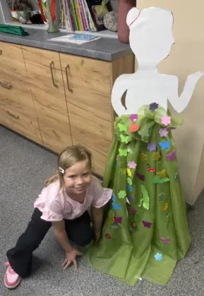 Uśmiechnięta dziewczynka kuca obok sukni pani wiosny.