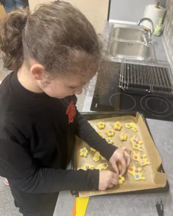 Dziewczynka wykrawa z ciasta ciasteczka kwiatuszki z cukiereczkami w środku.