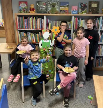 Sześcioro dzieci pozuje do wspólnego zdjęcia z panią wiosna na tle biblioteki.