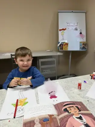 Uśmiechnięty chłopczyk koloruje kredkami obrazek.