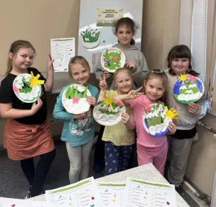 Uśmiechnięte dzieci po zajęciach trzymają swoje prace w rękach.