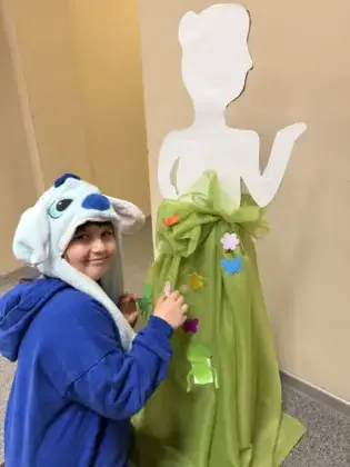 Uśmiechnięta dziewczynka przykleja ozdoby do sukni pani wiosny.